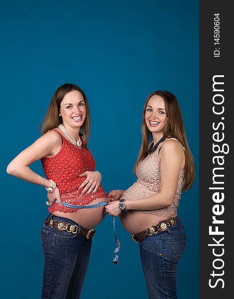 Two pregnant women (sister-twins) measuring belly, isolated. Two pregnant women (sister-twins) measuring belly, isolated