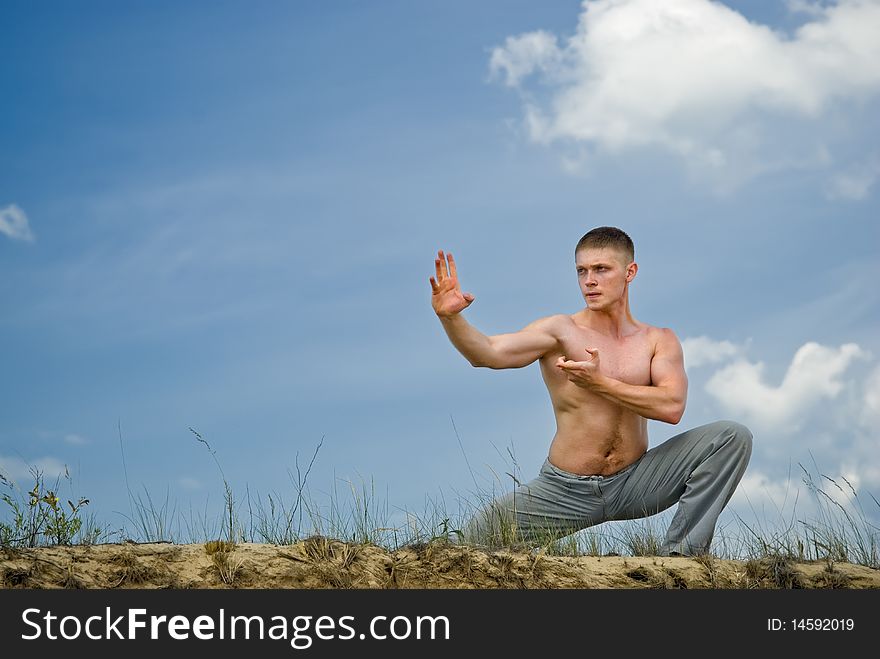 Young man in a karate pose in desert on cloudly sky background. Young man in a karate pose in desert on cloudly sky background