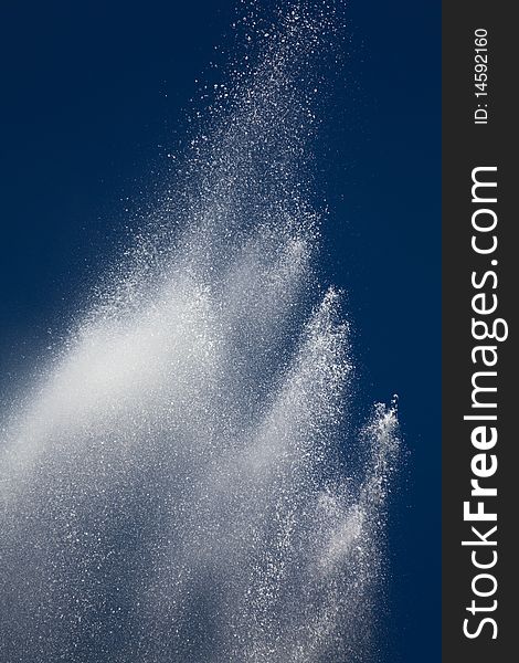 White splashes and drops of water from a fountain against the dark blue sky