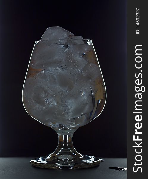 Transparent wineglass with ice and water on black background