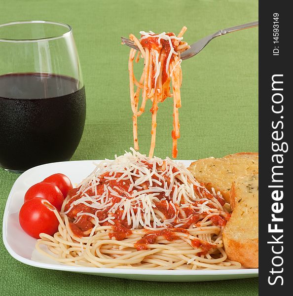 Spaghetti topped with sauce and grated cheese with garlic toast, cherry tomatoes and a glass of wine. Spaghetti topped with sauce and grated cheese with garlic toast, cherry tomatoes and a glass of wine