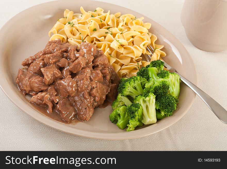 Beef tips topped with gravy with egg noodles and broccoli