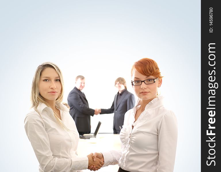 Two young business women are shaking hands in front of two business men. Image isolated on a light blue gradient background. Two young business women are shaking hands in front of two business men. Image isolated on a light blue gradient background.