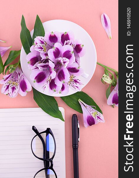 Fragrant tea in a white cup, beautiful flowers, a pink background, a notebook with a pen and glasses