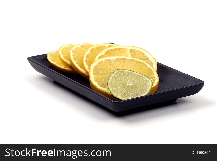 Slices of orange with a slice of lime on a black plate isolated against a white background. Slices of orange with a slice of lime on a black plate isolated against a white background.