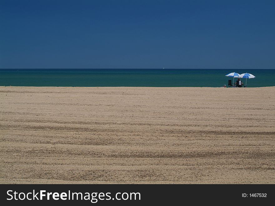 Two parasol and a couple alone on a desert beach