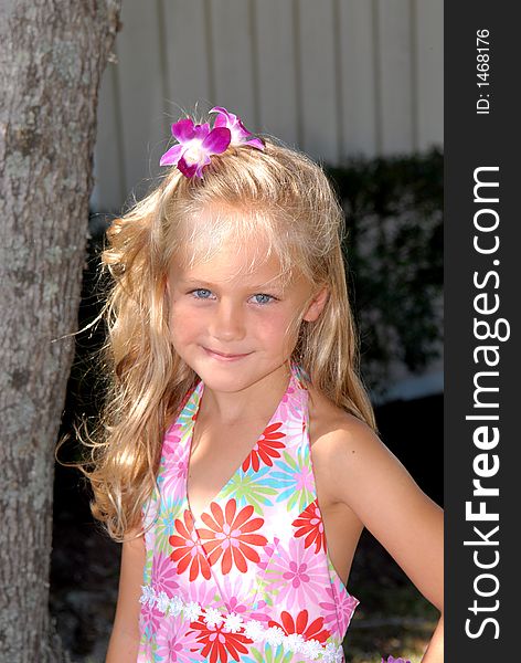 A beautiful little girl dressed in a tropical print dress with a flower in her hair and big blue eyes. A beautiful little girl dressed in a tropical print dress with a flower in her hair and big blue eyes.