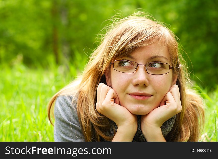 The young girl, in glasses, lays on a green grass, in park. The young girl, in glasses, lays on a green grass, in park