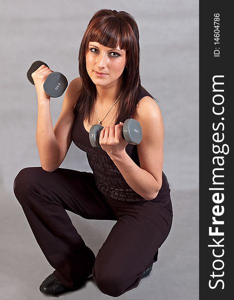 Young woman lifting weights on grey background