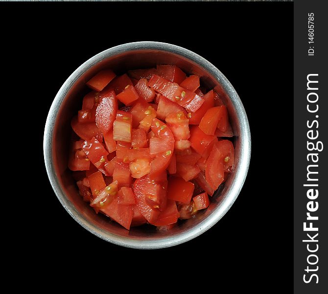 A bunch of sliced, diced, and cut red tomatoes inside of a round metal bowl isolated on pitch black background. A bunch of sliced, diced, and cut red tomatoes inside of a round metal bowl isolated on pitch black background.