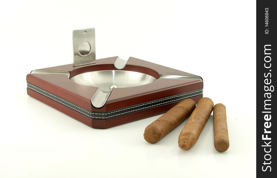 Elegant wood and metallic cigar ashtray with cigar cutter and cigars. Close-up. Elegant wood and metallic cigar ashtray with cigar cutter and cigars. Close-up.