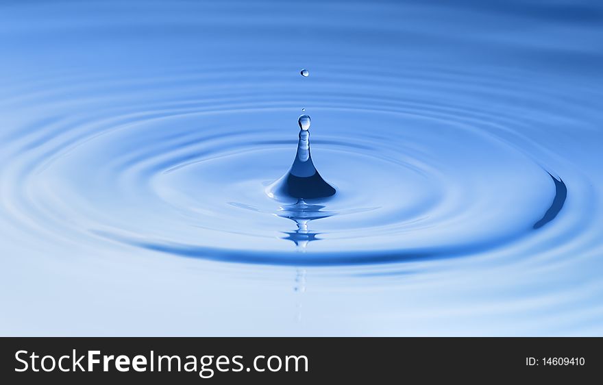 Clean blue drop of water splashing in clear water. Abstract blue background