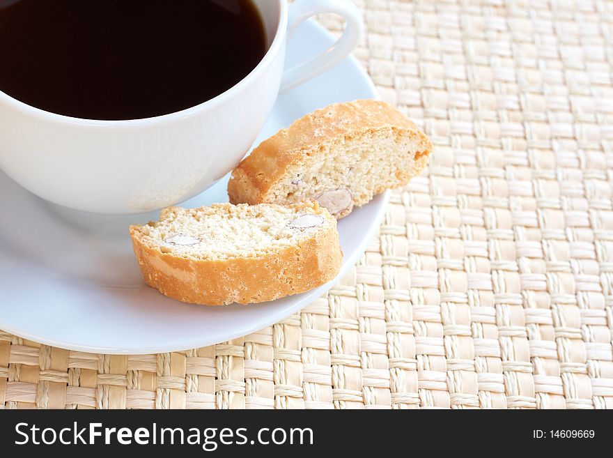 Cup of hot black coffee and baked almond biscotti cookies on woven straw placemat. Cup of hot black coffee and baked almond biscotti cookies on woven straw placemat