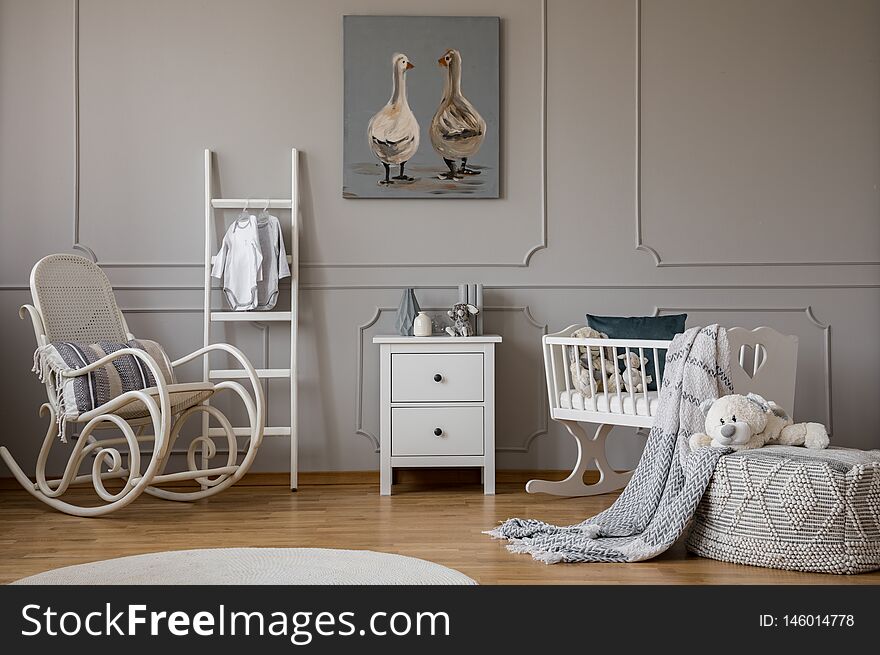 White wooden rocking chair with pillow next to scandinavian ladder, chest of drawers and cradle, copy space on wall with cute