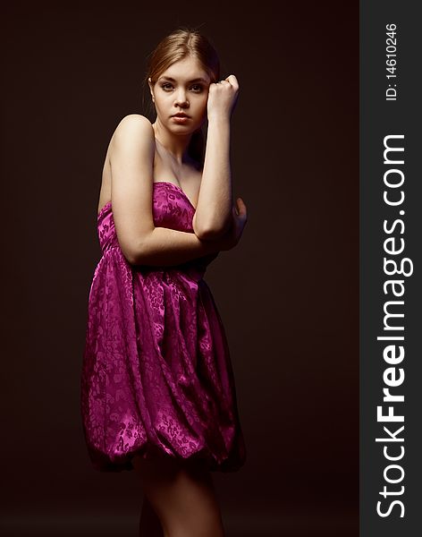 Seductive young woman wearing pink dress on a dark background