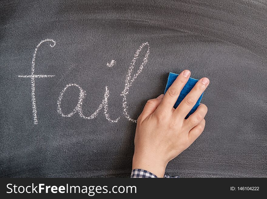 A woman`s hand with a sponge erases the chalk-written word fail from the blackboard. the concept of success, forget failure