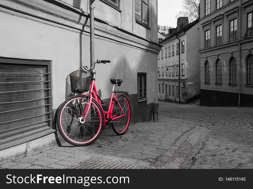 A picture of a lonely red bike standing in the typical street in Stockholm. The bike looks to be modern in a retro style. The background is black and white.