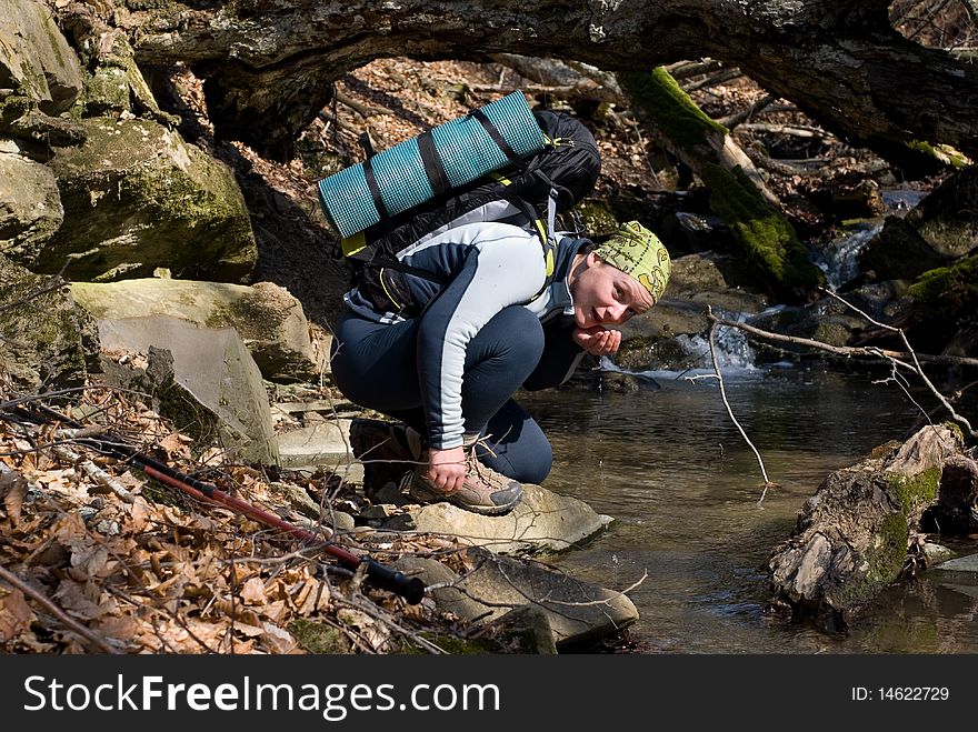 A smiling woman drinks water from a forest stream. Spring in the Crimean mountains. A smiling woman drinks water from a forest stream. Spring in the Crimean mountains