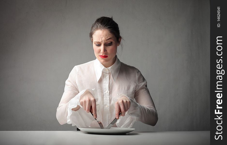 Woman with doubtful expression using fork and knife on an empty dish. Woman with doubtful expression using fork and knife on an empty dish