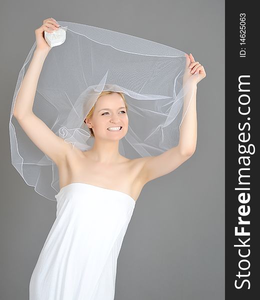 Young beautiful bride covered in veil.gray background