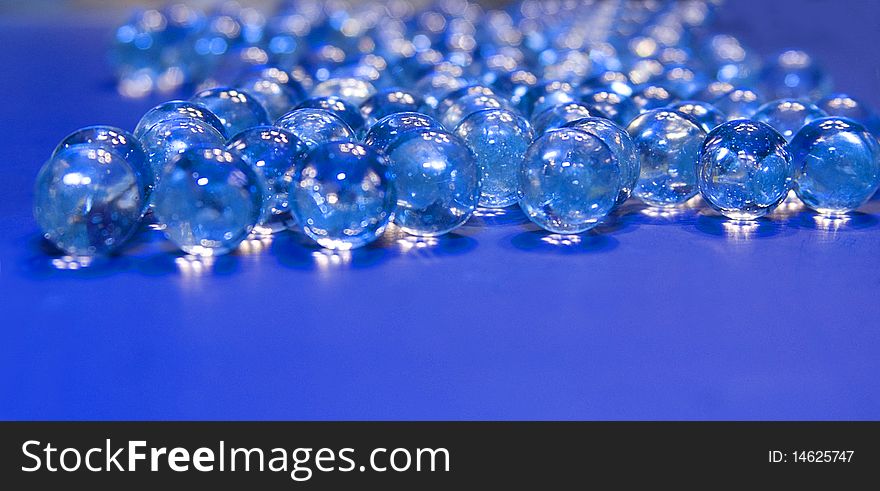 Many clear marbles laying on blue board. Many clear marbles laying on blue board