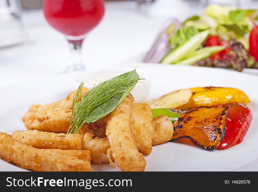 Fried calamari seafood meal with salad on a white plate with a fresh fruit drink