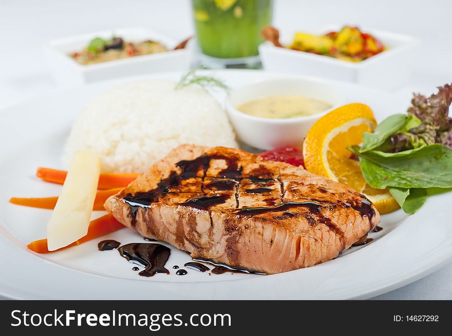 A la carte salmon steak meal on a white plate with salad and rice. A la carte salmon steak meal on a white plate with salad and rice