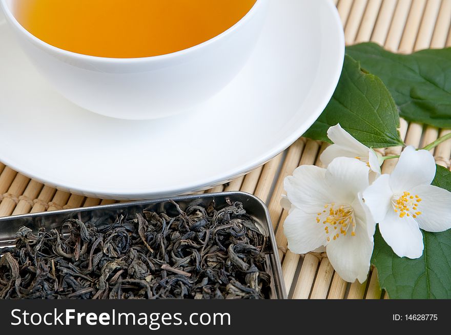 A cup of tea on a tray with dried tea and jasmine branch. A cup of tea on a tray with dried tea and jasmine branch