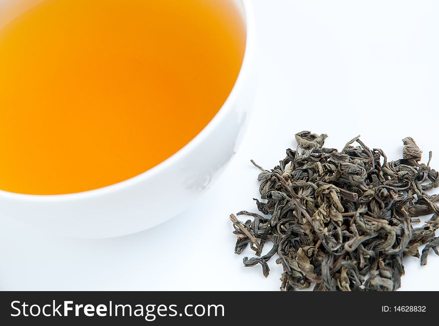 A cup of tea on a tray with dried tea leaves, isolated on white