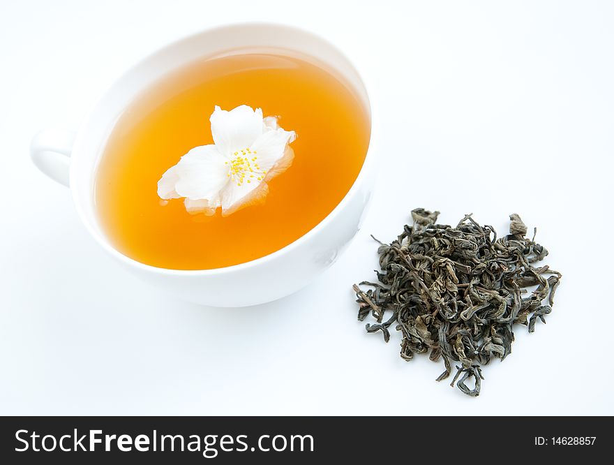 A cup of tea on a tray with dried tea leaves and jasmine flower, isolated on white