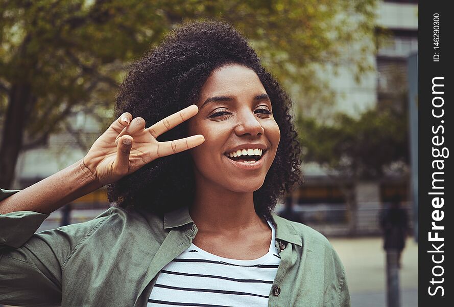 Portrait of a happy young woman standing outdoor looking at camera showing peace gesture. Portrait of a happy young woman standing outdoor looking at camera showing peace gesture