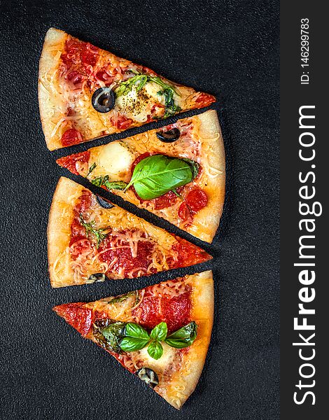 Slices of pizza with  pepperoni and basil leaf  with spices on black background, copy space. Flatbread pizza. Top view