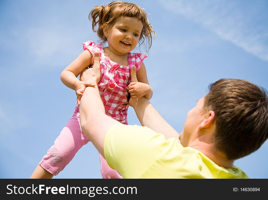 Young happy dad playfully tosses his little daughter in the sky in the sky. Young happy dad playfully tosses his little daughter in the sky in the sky