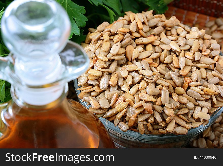 Oil from sunflower seeds in a glass bottle with the cleared sunflower seeds and a parsley branch.