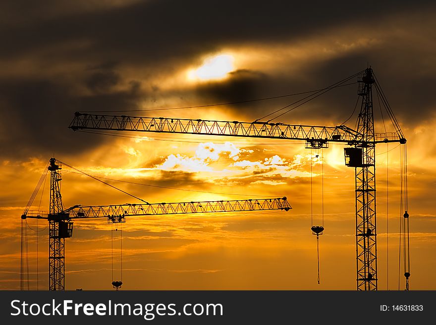Contours of building cranes against the sunset sky
