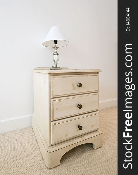 Detail of a wooden bedside table with three drawers and bedside lamp