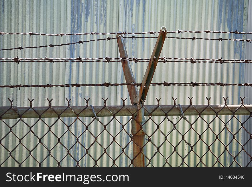 Detail of fencing with barbed wire. Corrugated metal siding in the background.