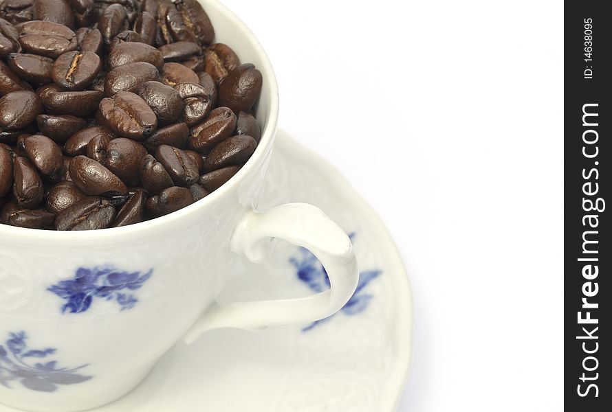 Roasted coffee beans fill china cup and saucer. Roasted coffee beans fill china cup and saucer