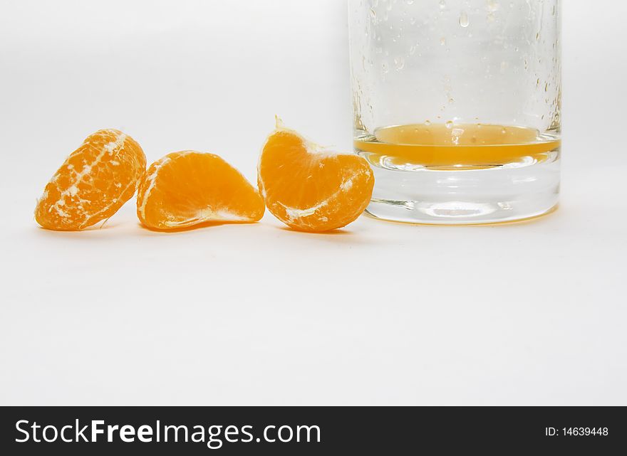 The segments of a tangerine lying near a glass with natural orange juice. The segments of a tangerine lying near a glass with natural orange juice