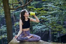 Healthy Fitness Girl Sitting In Lotus Pose And Drinking Water From Green Bottle In Forest Royalty Free Stock Photography