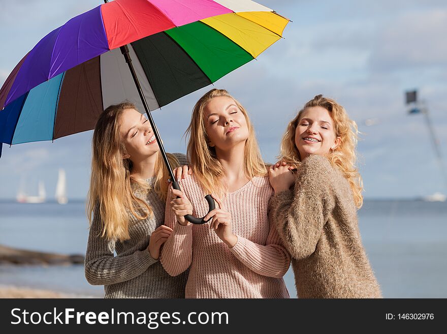 Three pretty young women friends under colorful umbrella parasol. Fashionable females wearing sweaters spending time outdoor. Three pretty young women friends under colorful umbrella parasol. Fashionable females wearing sweaters spending time outdoor