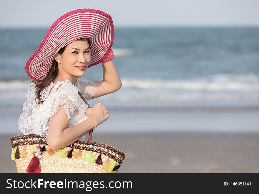 Woman carry big handcraft bag wearing beautiful hat standing and looking to camra with wave and background. Process in retro film style. Woman carry big handcraft bag wearing beautiful hat standing and looking to camra with wave and background. Process in retro film style