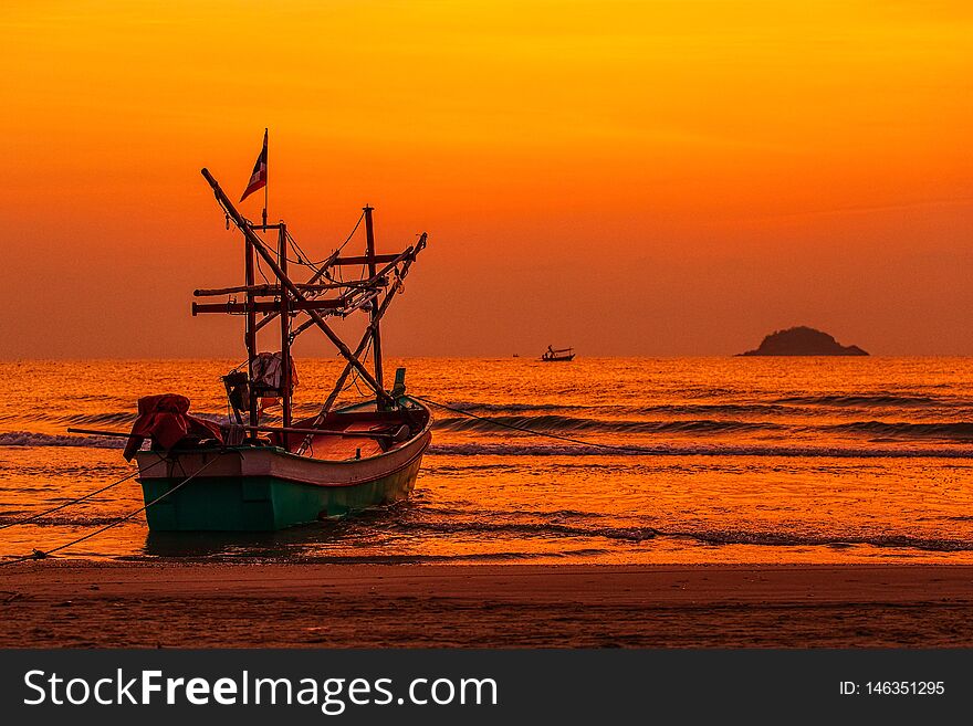 Native Thai style fishery boat anchored on beach in the morning light with island  and colorful sky in background