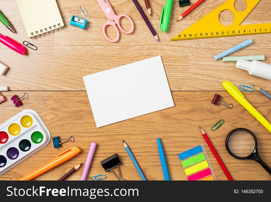 School supplies on wooden table, background with frame made of stationery and blank paper card in center. Education, studying and back to school concept. Child desk top view, copy space, flat lay