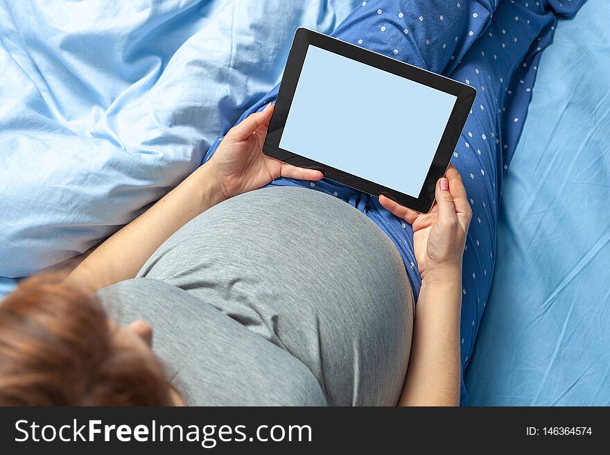 Pregnant Woman With Belly Holds Tablet In Hands.