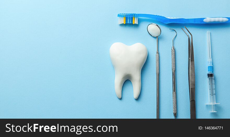 Tooth and dental instruments on blue background. Dental treatment. Dentist tools mirror, hook, tweezers, syringe and toothbrush. Copy space for text
