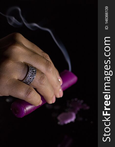 A woman`s hand with a beautiful silver ring holds a smoking purple candle.
