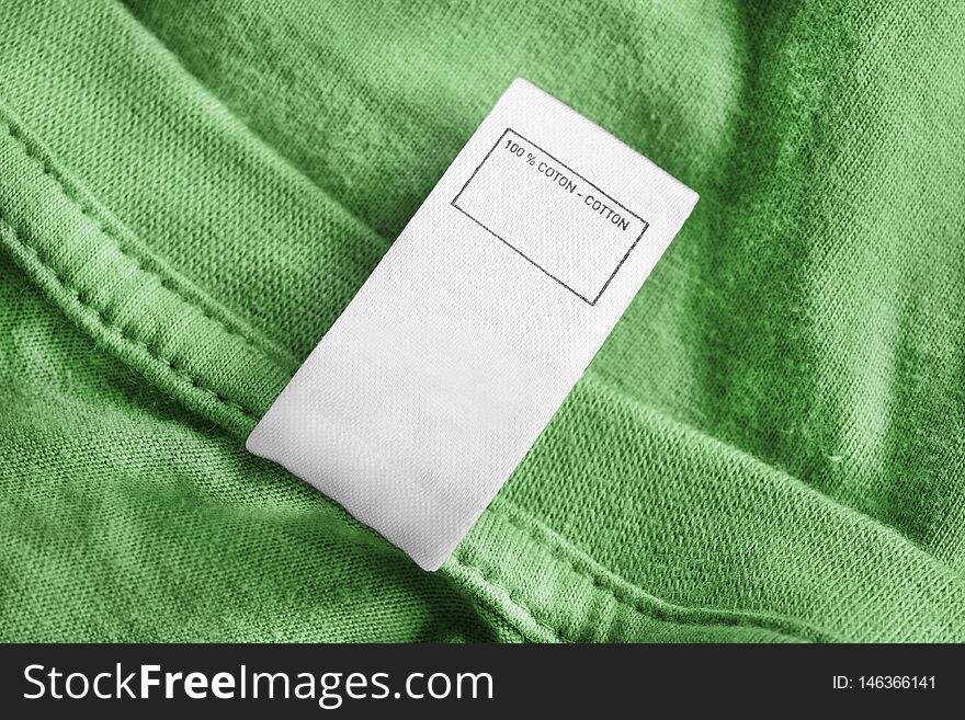 Clothes label says 100% cotton on green textile background. Clothes label says 100% cotton on green textile background