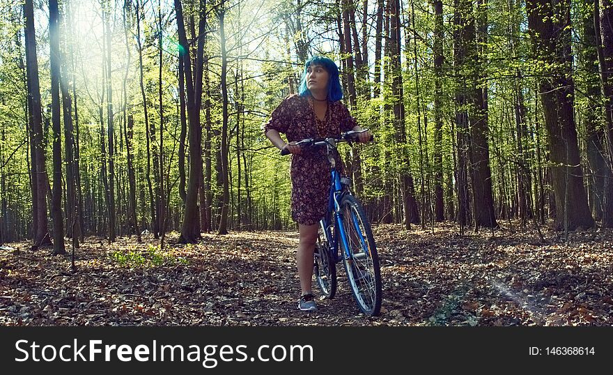 The girl with blue hair in the dress rides a bicycle through the forest. The girl with blue hair in the dress rides a bicycle through the forest.