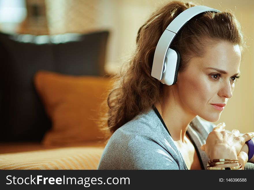 Portrait of pensive active woman in sport clothes listening to the music with headphones in the modern house. Portrait of pensive active woman in sport clothes listening to the music with headphones in the modern house